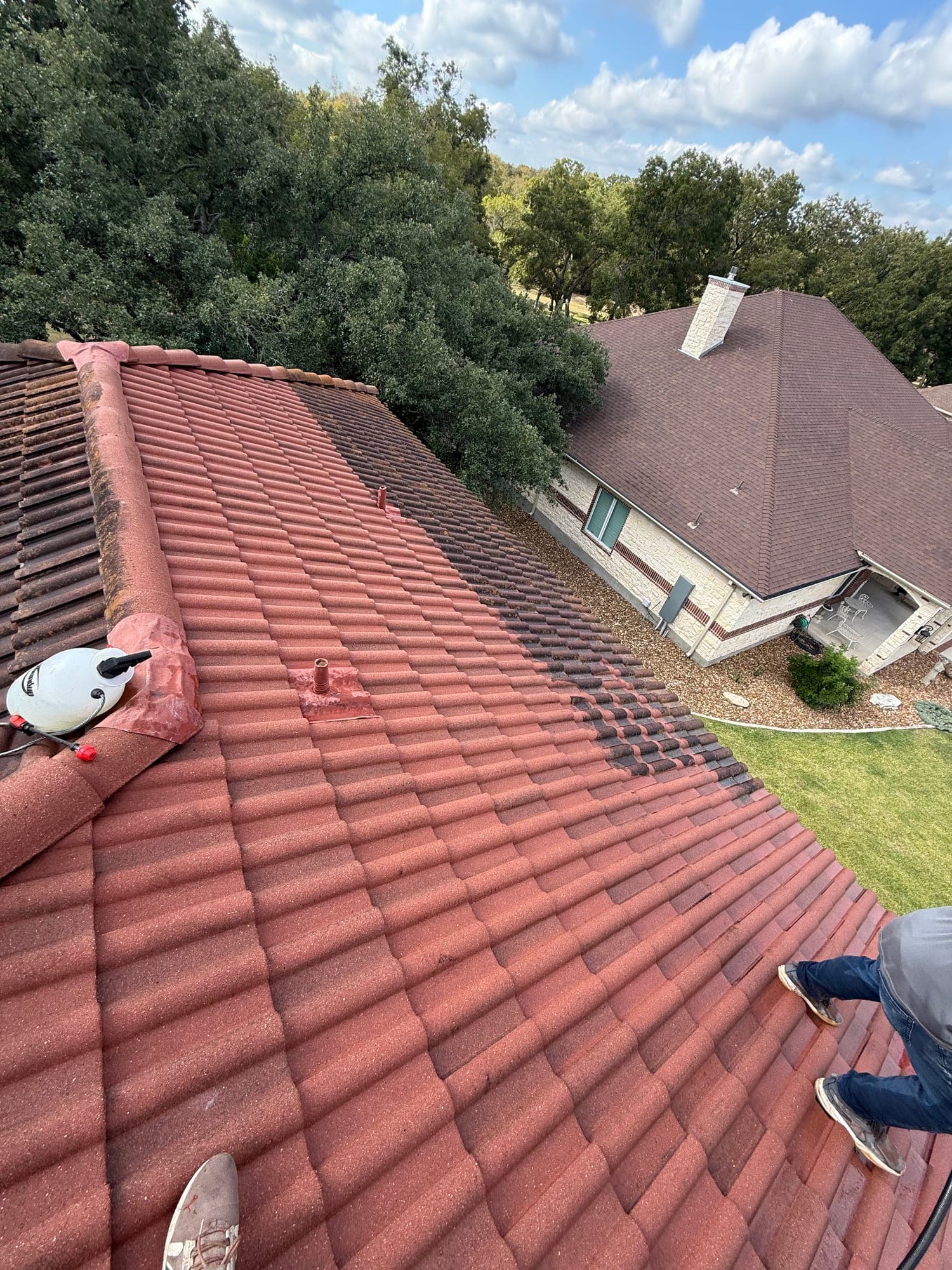 A red barrel tile roof mid-clean: the near half washed back to bright terracotta, the far half still dark with algae growth