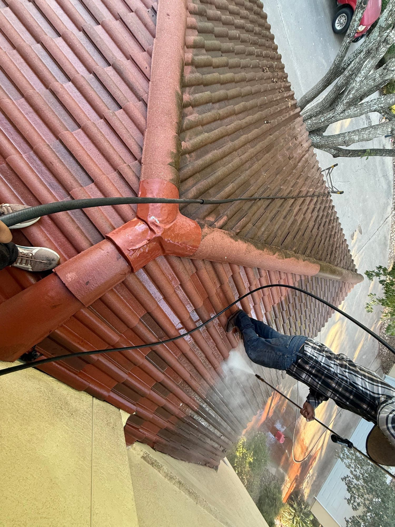 A soft wash wand rinsing a clay tile roof at low pressure, water running down the courses
